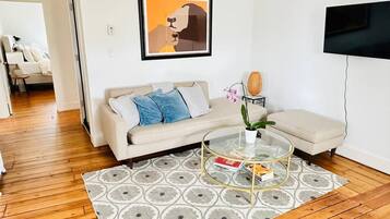 Un salon avec un canapé, une table basse en verre, un téléviseur et une œuvre d’art encadrée accrochée au mur.