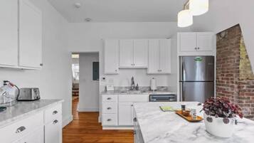 A modern kitchen with white cabinetry, a marble countertop, and a stainless steel refrigerator.