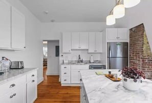 A modern kitchen with white cabinetry, a marble countertop, and a stainless steel refrigerator. - Modern Penthouse with Partial Ocean Views (Newport)