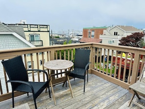 Een houten terras met twee stoelen en een tafel, met uitzicht op een woonwijk.