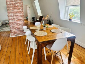 A dining area with a wooden table, white chairs, and woven placemats. - Modern Penthouse with Partial Ocean Views (Newport)