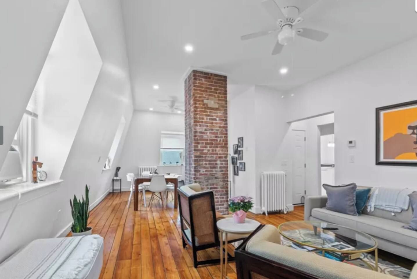 A modern living room with a dining area, a brick column, and a ceiling fan.