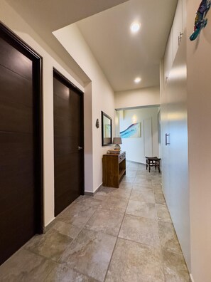 Corredor com porta de madeira escura, um banco de madeira e uma mesa com abajur.