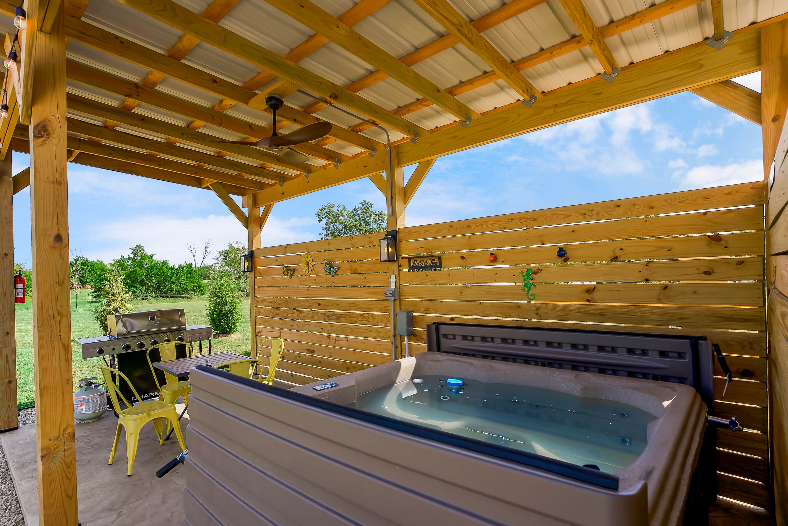 Een overdekt buitengebied met een jacuzzi, een barbecue en gele stoelen.