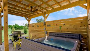 Een overdekt buitengebied met een jacuzzi, een barbecue en gele stoelen.