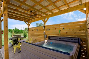 A covered outdoor area with a hot tub, a grill, and yellow chairs.