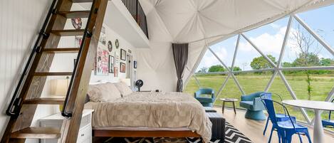 A bedroom with a bed, a dresser, a chair, and a table. There is a ladder leading to a loft area with a window.