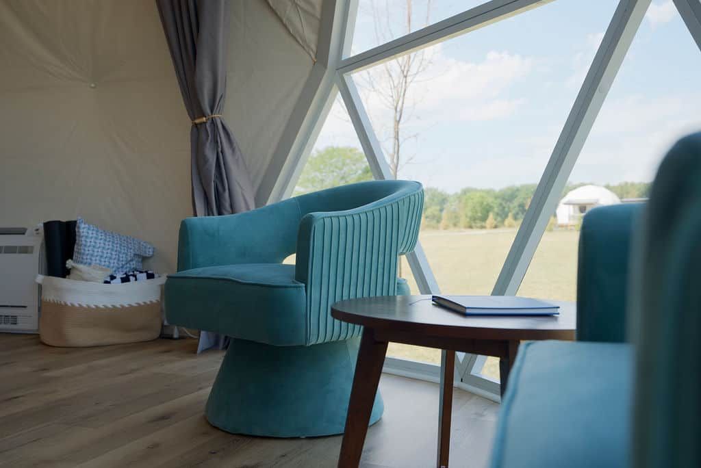 A tent with a view of a landscape, a blue chair, a small table, and a basket with clothes.