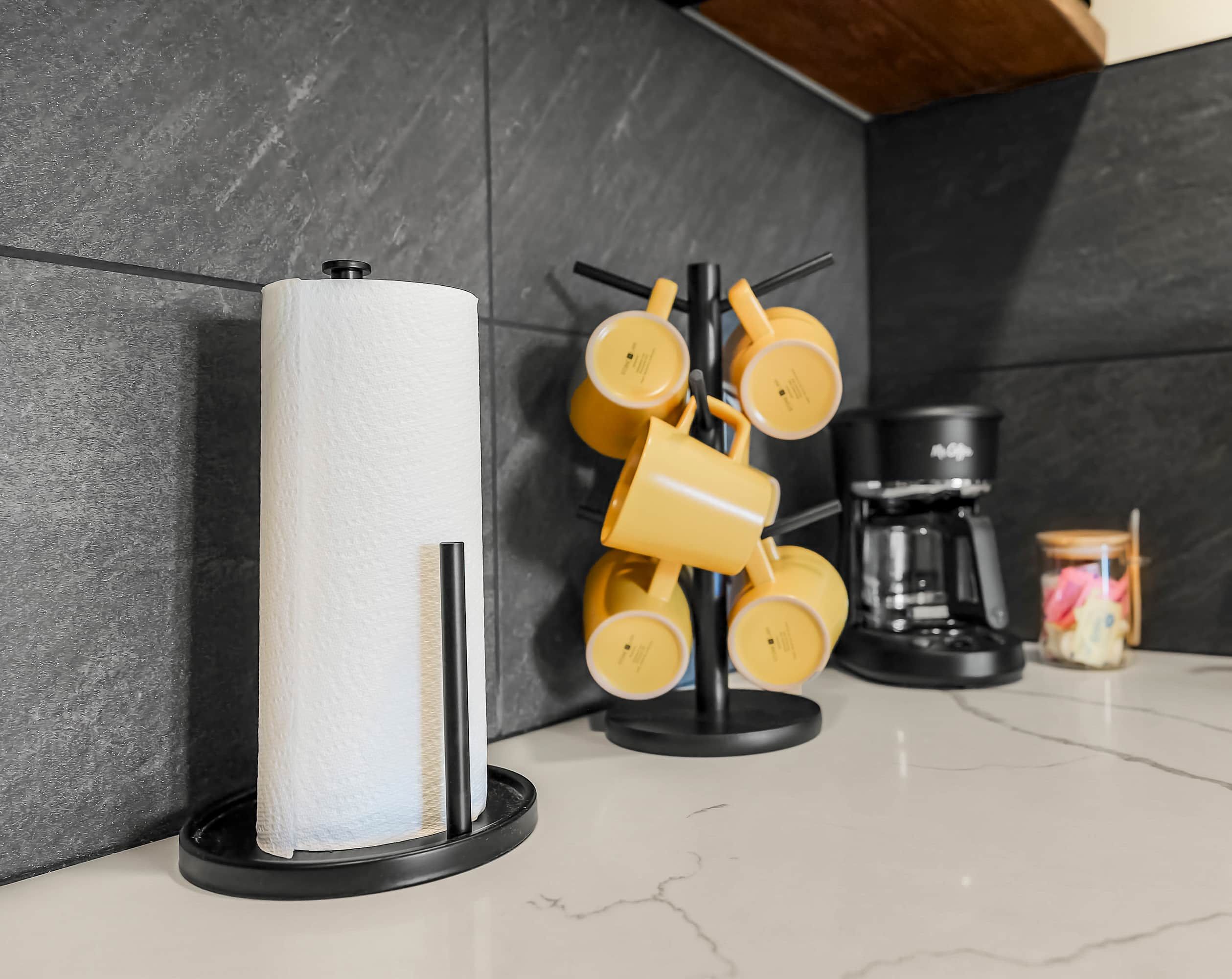 A kitchen with a paper towel holder, a coffee maker, and a jar of snacks.