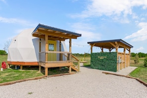 Two geodesic domes with wooden decks and a gazebo, set in a grassy area with a clear sky.