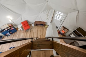 A tented accommodation with a wooden staircase, a red sofa, and a desk with a lamp.