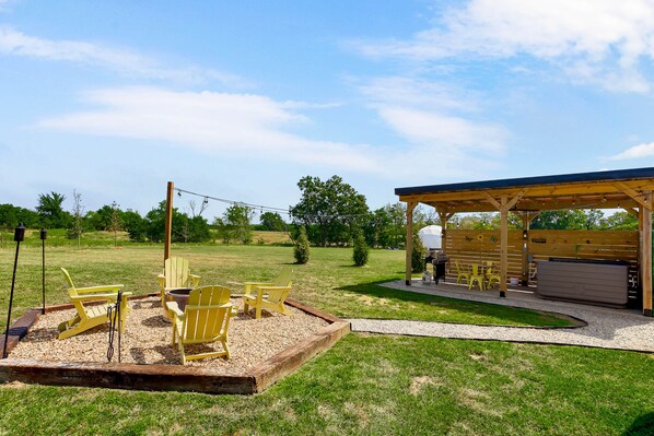 Un espacio de estar al aire libre con sillas Adirondack, una parrilla y un pabellón cubierto.