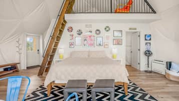 A bedroom with a loft area, a bed, a bench, a chair, and a fan.