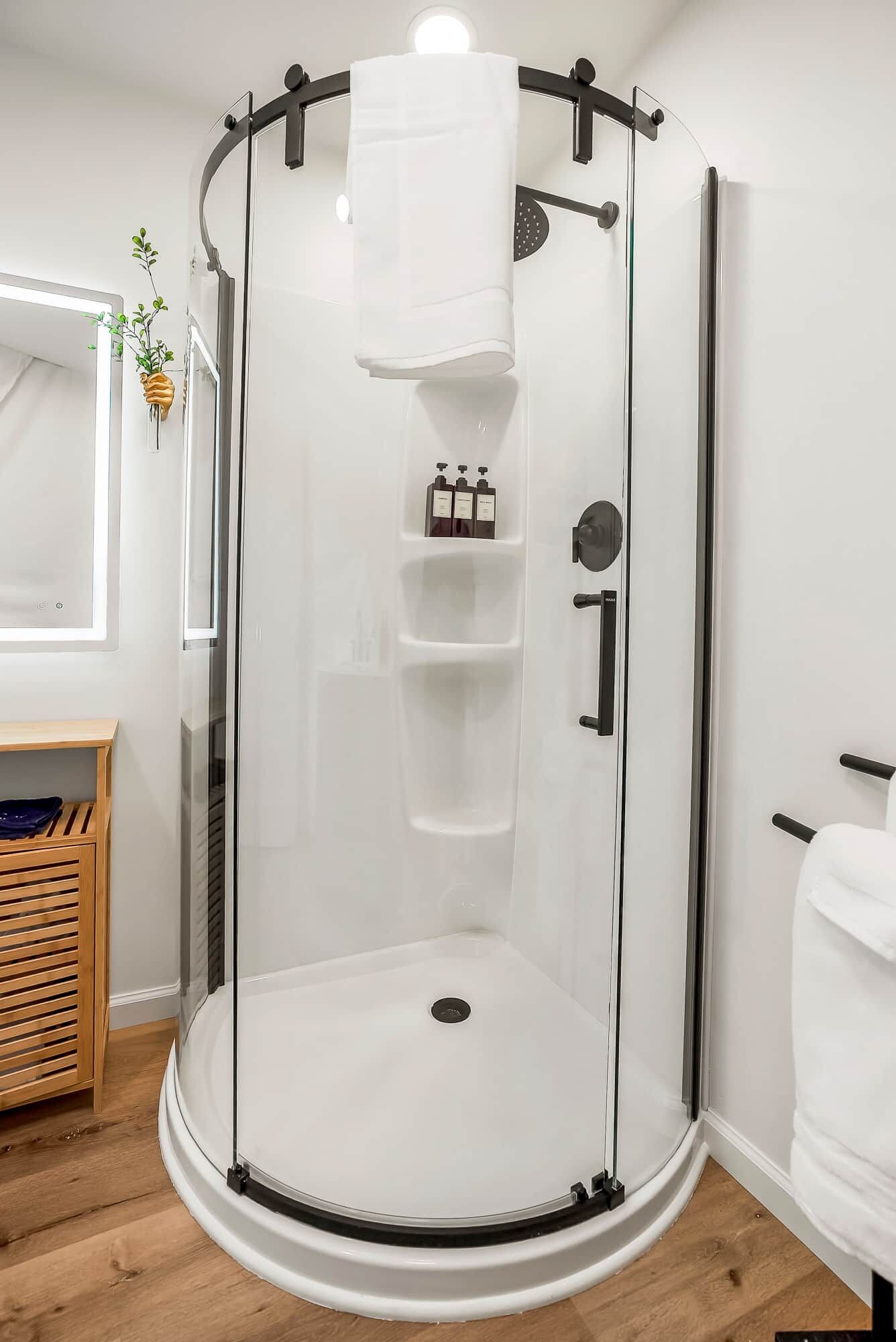 A glass-enclosed shower area with a white interior, a towel rack, and a shelf with toiletries.