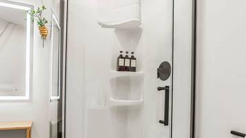 A glass-enclosed shower area with a white interior, a towel rack, and a shelf with toiletries.