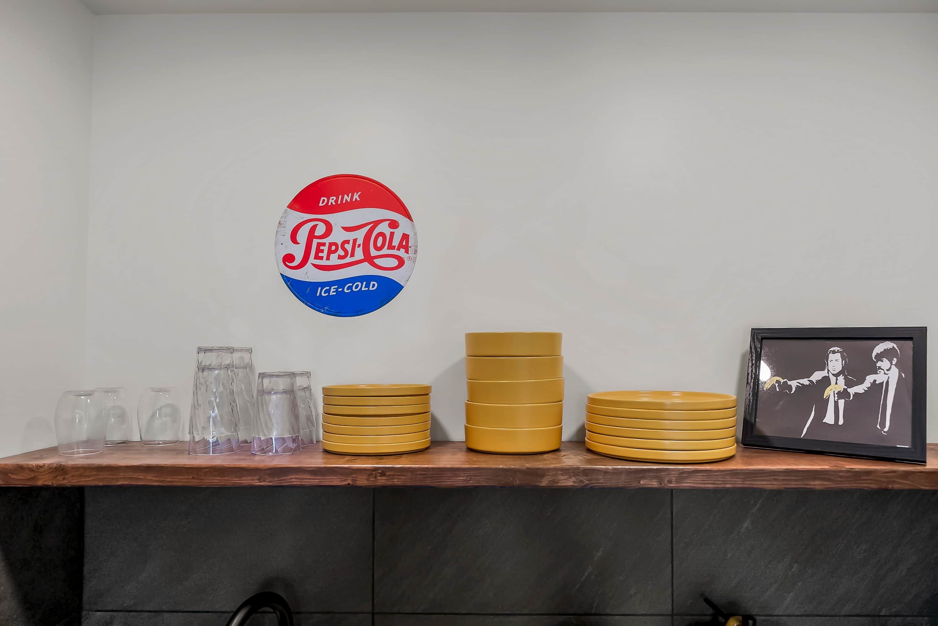 A bar area with a Pepsi-Cola sign, stacked yellow plates, and clear glasses.