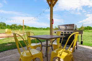An outdoor patio with a grill, yellow chairs, and a table.