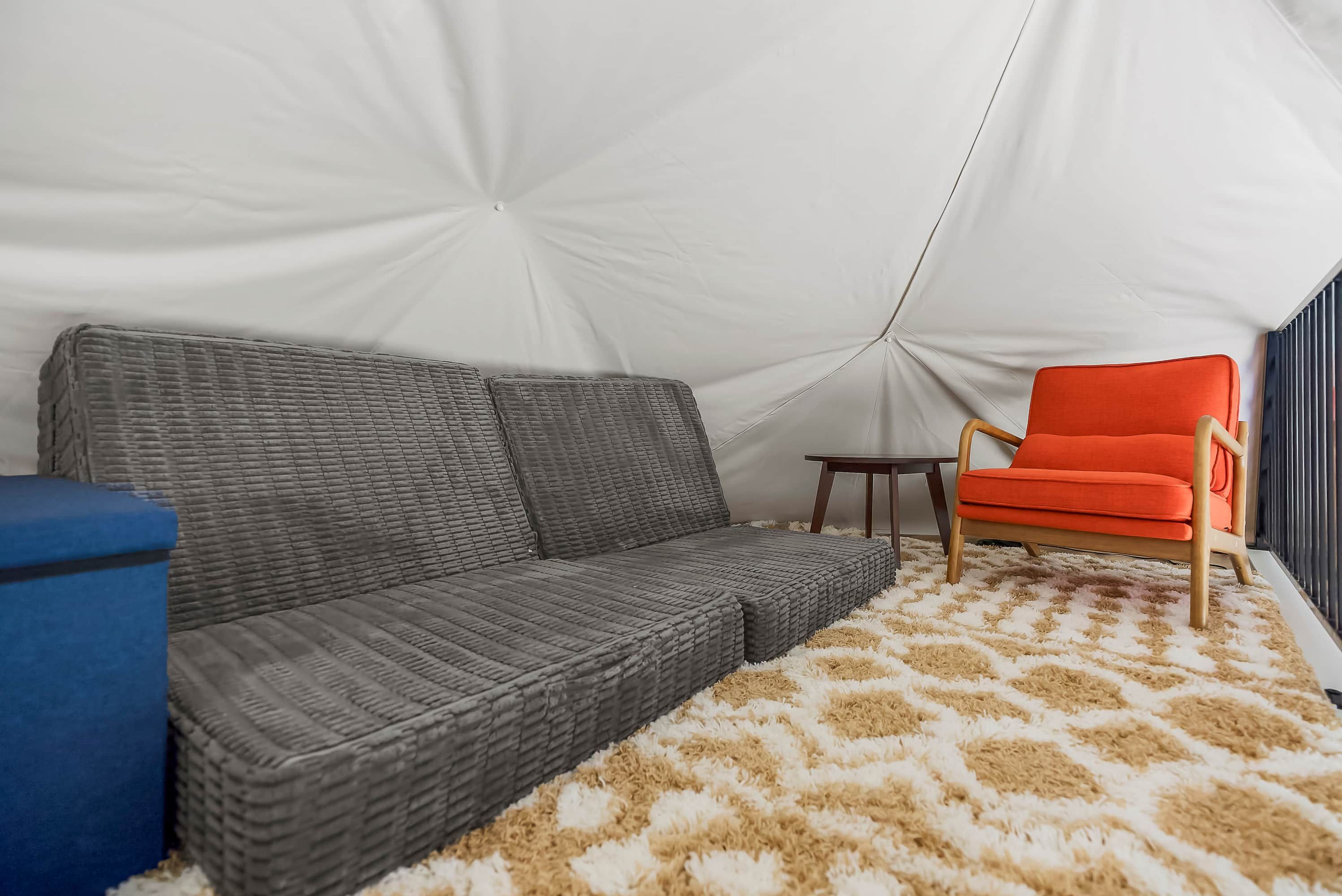 Een tent van binnen, met een grijze bank, een klein tafeltje en een feloranje stoel.