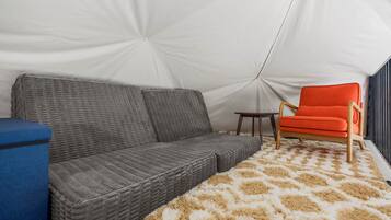 Een tent van binnen, met een grijze bank, een klein tafeltje en een feloranje stoel.