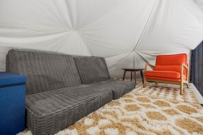 Ein Zeltinneres mit einem grauen Sofa, einem kleinen Tisch und einem leuchtend orangefarbenen Sessel.