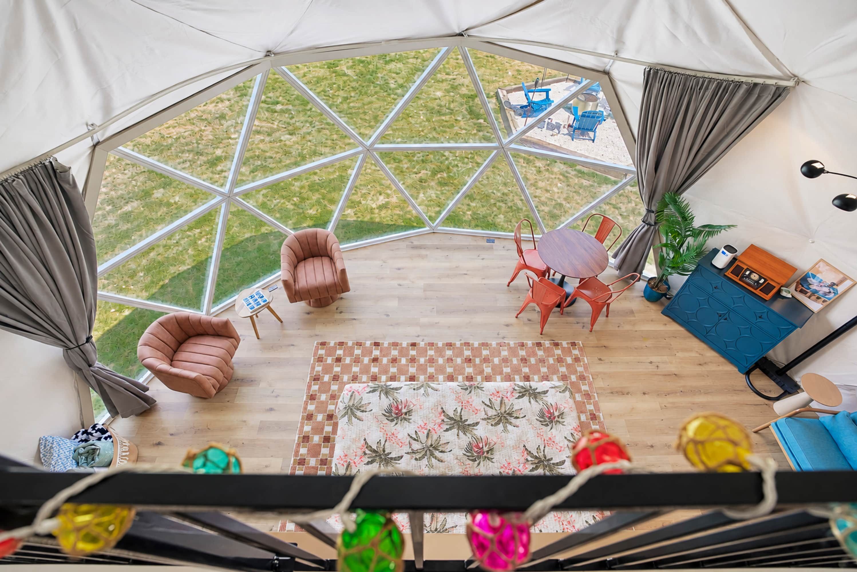 A tent with a geometric window design, a wooden floor, a central seating area with chairs, a small table, and a blue cabinet with a radio.