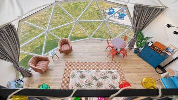 A tent with a geometric window design, a wooden floor, a central seating area with chairs, a small table, and a blue cabinet with a radio.