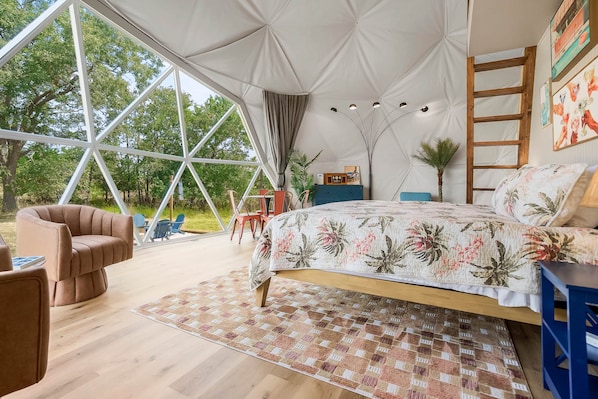 A spacious tented room with a large bed, a chair, and a view of the outdoors.