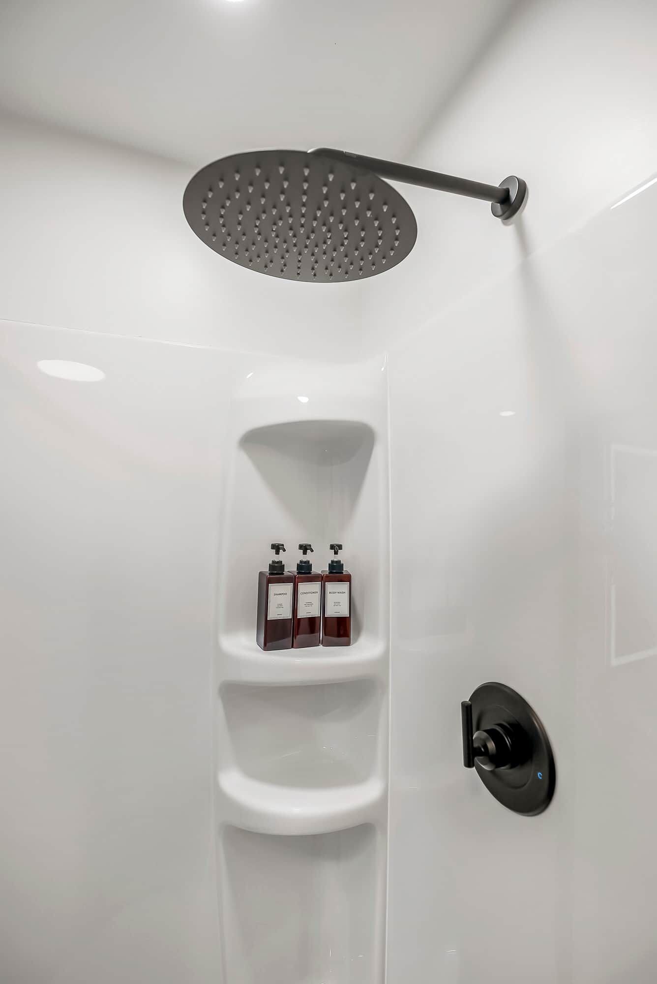 A shower area with a rain showerhead, a soap dispenser, and a hand dryer.