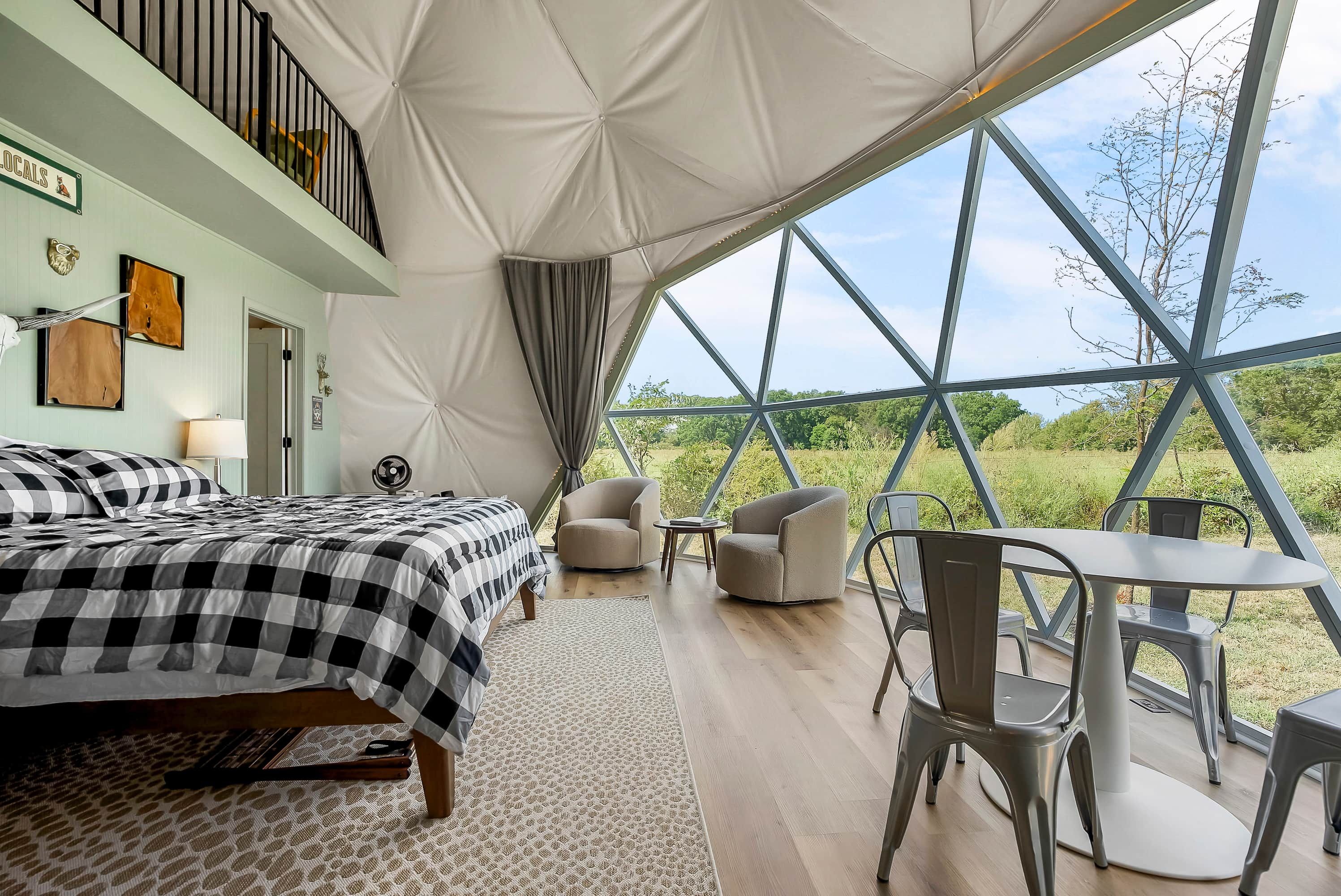 Ein Zelten-ähnliches Zimmer mit einem Bett, Stühlen, einem Tisch und Blick ins Grüne.