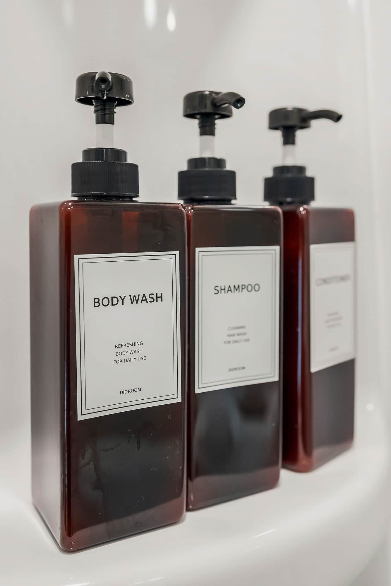 Trois flacons de gel douche et de shampoing dans un récipient blanc.
