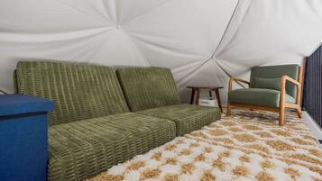 Een tent van binnen, met een groene bank, een houten stoel en een kamerkleed met een patroon.