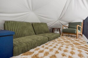 L'intérieur d'une tente avec un canapé vert, une chaise en bois et un tapis à motifs.