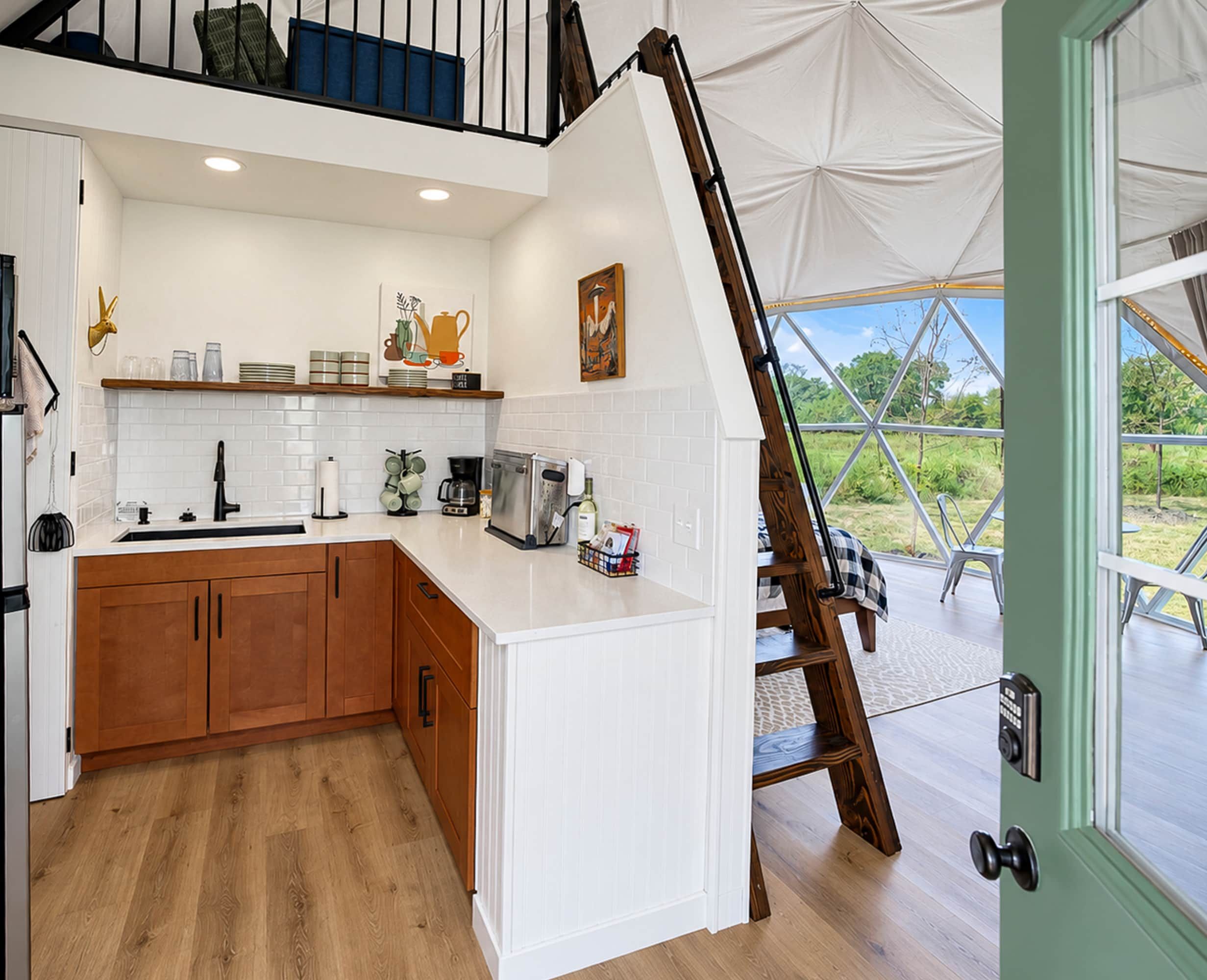 Une cuisine moderne avec des meubles blancs, un plan de travail en bois et un coin repas offrant une vue sur la verdure.