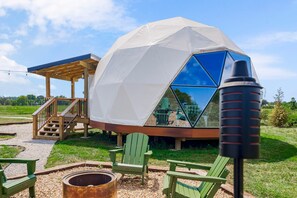 A geodesic dome structure with a wooden deck, outdoor seating, and a fire pit.