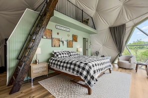 A bedroom with a bed, a nightstand, a lamp, a chair, a fan, and a sign on the wall.