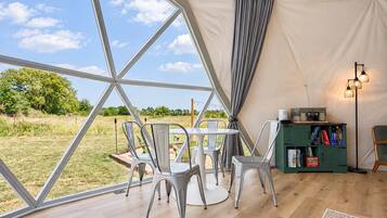 Een tent met een tafel, stoelen, een boekenkast en uitzicht op de natuur.