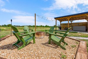 An outdoor seating area with Adirondack chairs and a fire pit, surrounded by gravel.