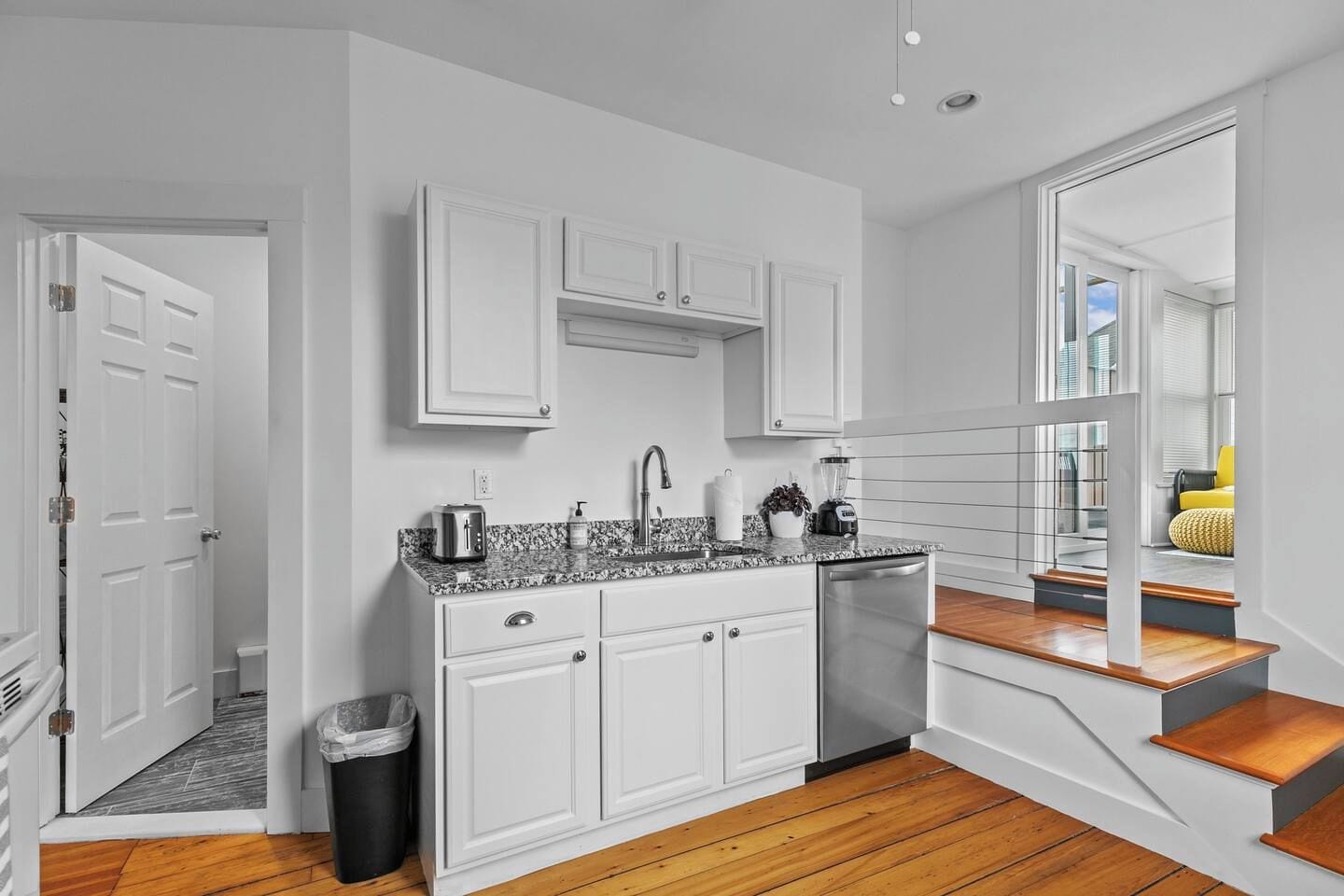 A modern kitchen with white cabinetry, a granite countertop, and a stainless steel dishwasher.