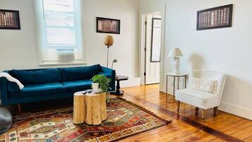 Un salon avec un canapé bleu, un fauteuil blanc, un tapis à motifs et une table basse en bois.