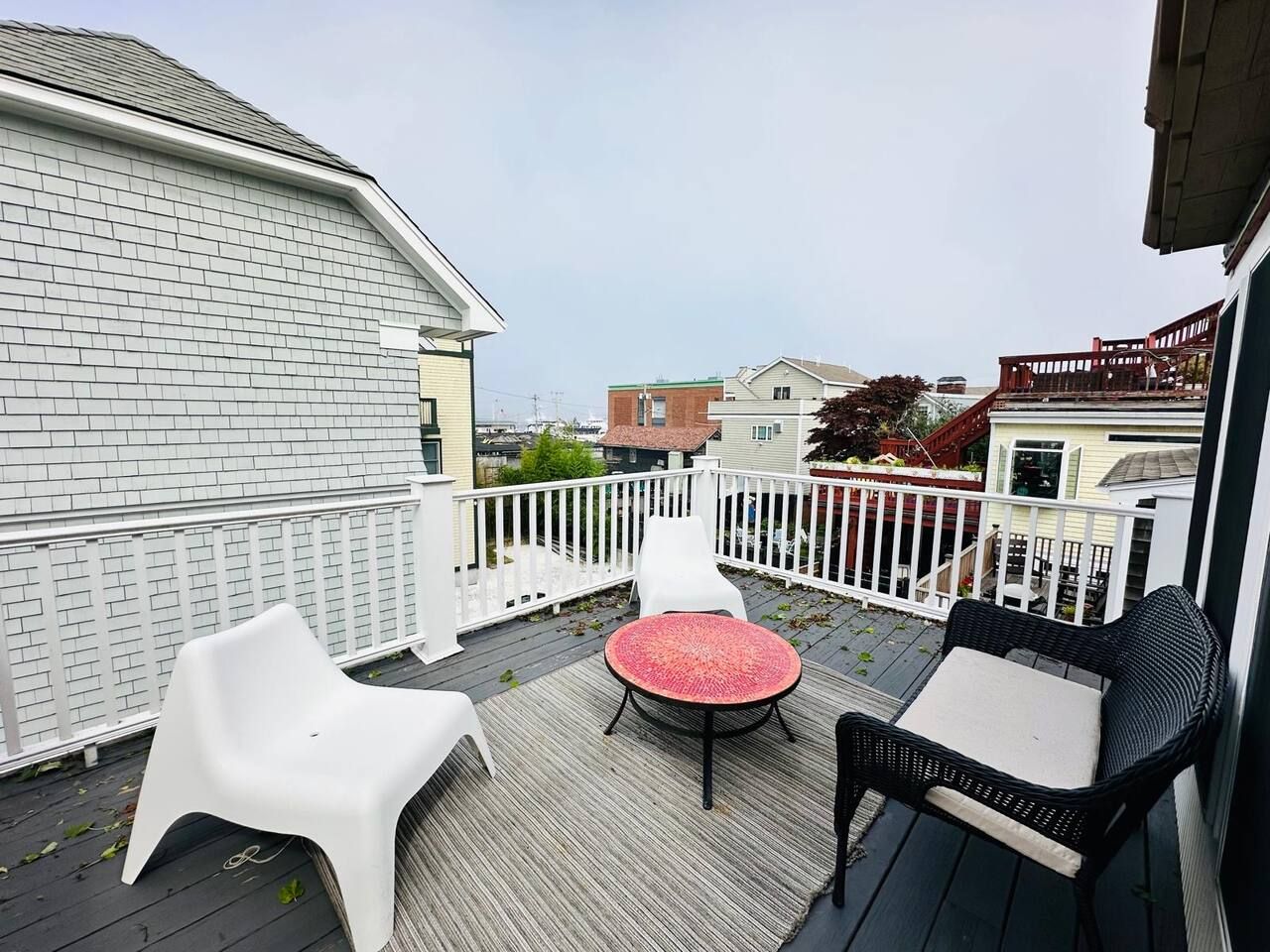 Une terrasse avec une table ronde et deux chaises, une clôture blanche et un bâtiment en arrière-plan.