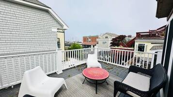 Une terrasse avec une table ronde et deux chaises, une clôture blanche et un bâtiment en arrière-plan.