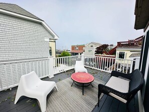 Eine Terrasse mit einem runden Tisch und zwei Stühlen, ein weißer Zaun und ein Gebäude im Hintergrund.
