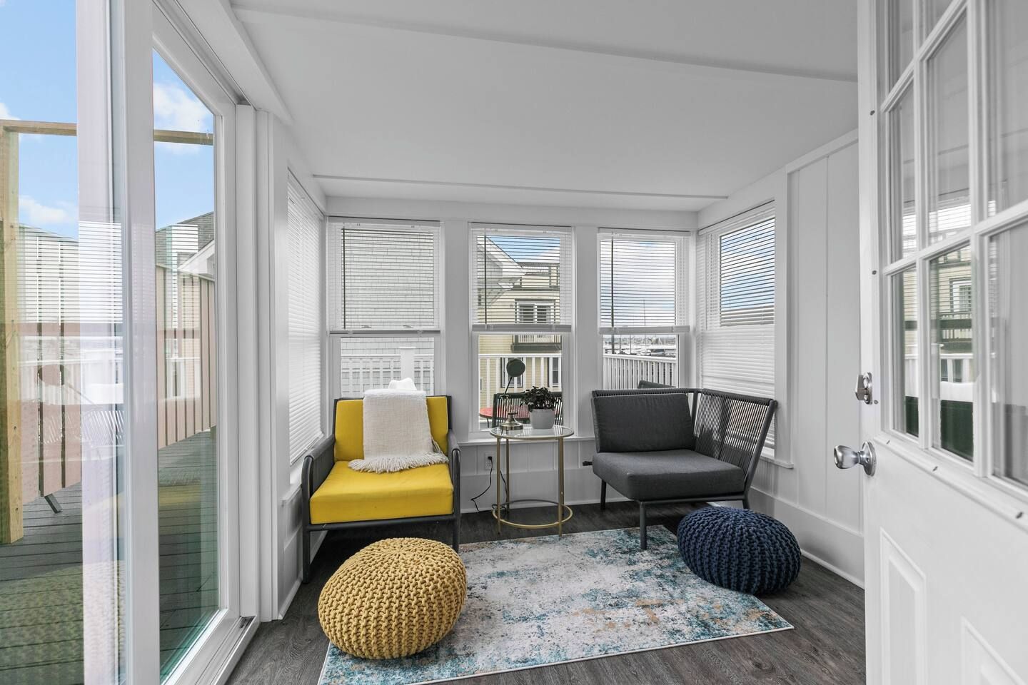 A sunroom with a yellow chair, a gray chair, a small table, and a round ottoman.