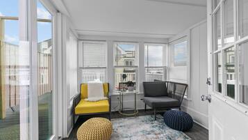 A sunroom with a yellow chair, a gray chair, a small table, and a round ottoman.