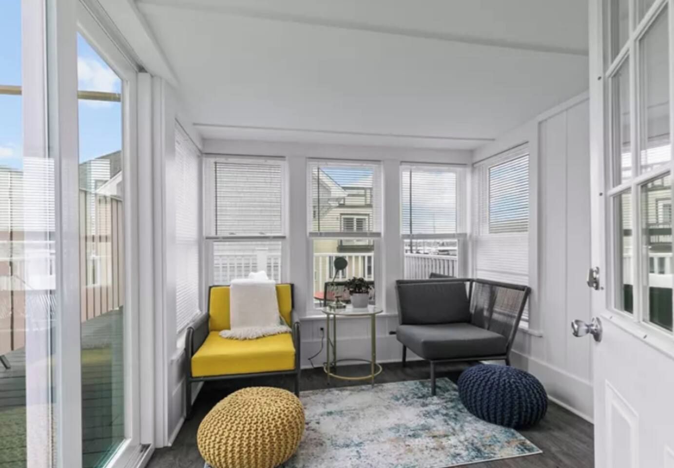 A sunroom with a yellow sofa, a gray chair, and a small table with a plant.