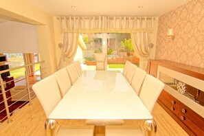 A dining area with a long table, chairs, and a view of a garden. - CT 233 - 1001 Nights - 1001 Nights - CT 233 (Benalmadena)
