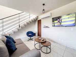 Uma sala de estar moderna com escada, um sofá, uma mesa de centro e uma TV fixada na parede.