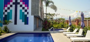 Une piscine avec des chaises longues et une fresque murale aux couleurs vives.