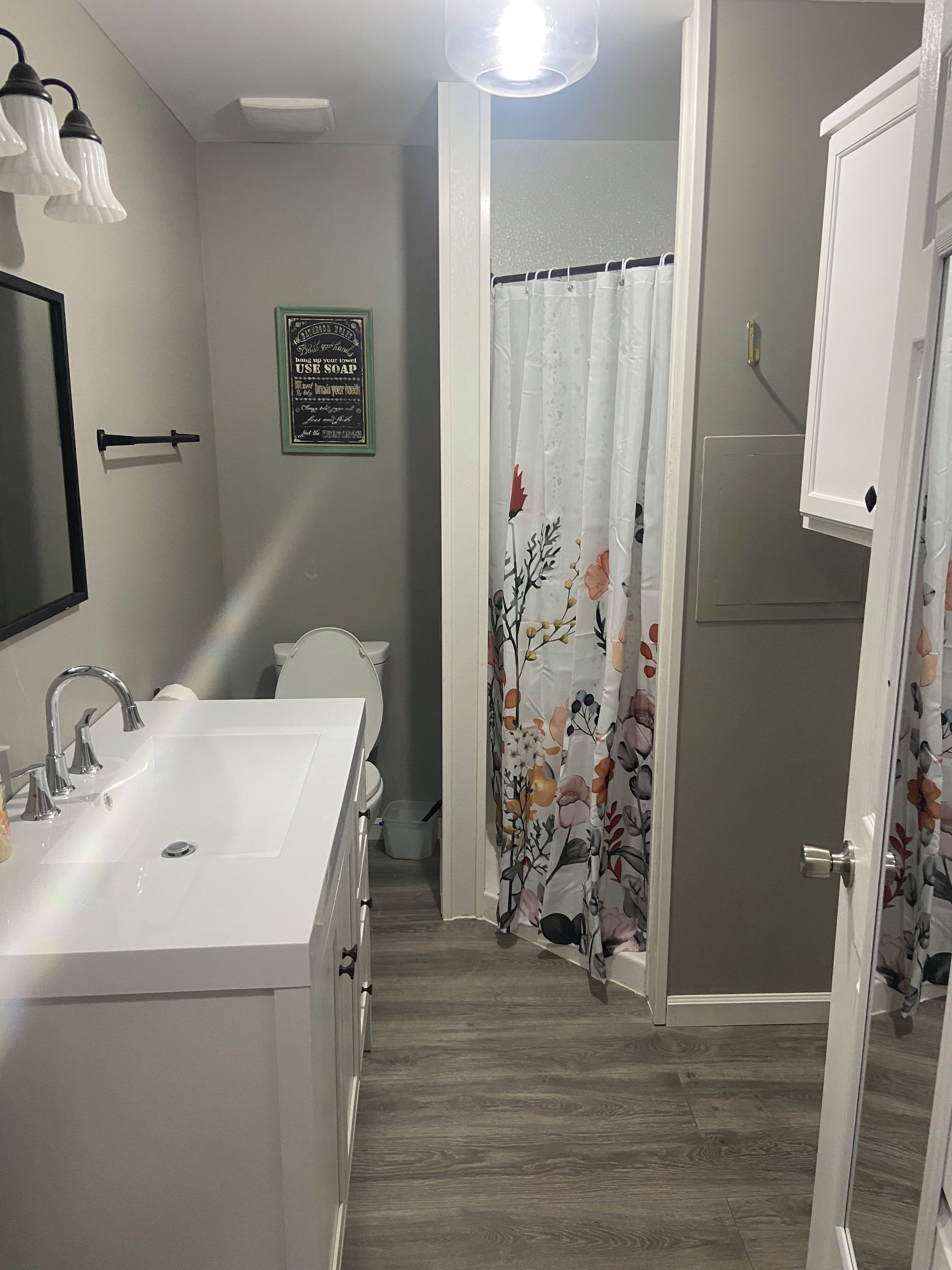 Un baño con lavamanos blanco, inodoro y cortina de ducha con motivos florales.