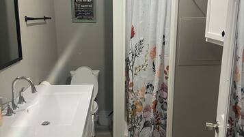 Un baño con lavamanos blanco, inodoro y cortina de ducha con motivos florales.